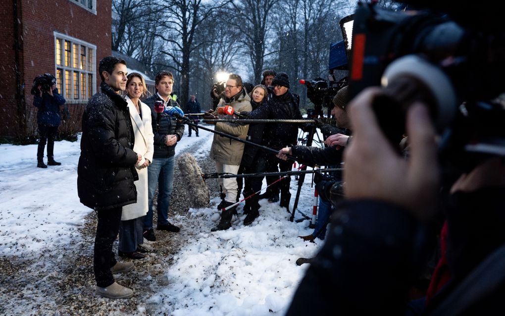 De drie onderhandelaars staan met winterjassen aan voor draaiende camera’s de pers te woord. Ondertussen dwarrelt de sneeuw neer.