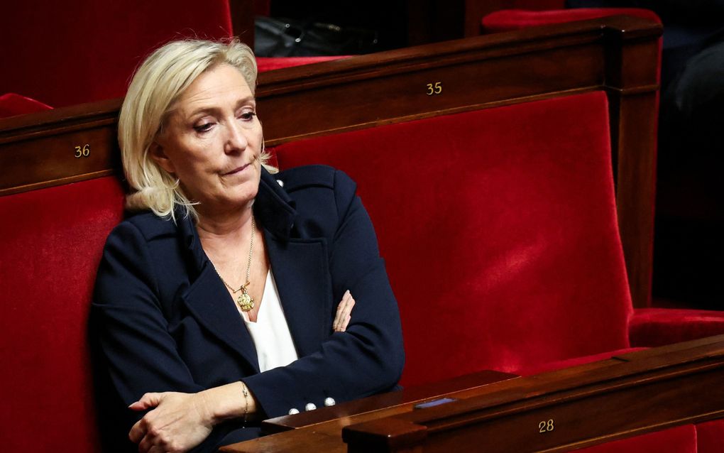 Vrouw met blond haar en blauwe kleren zit in een rood bankje.