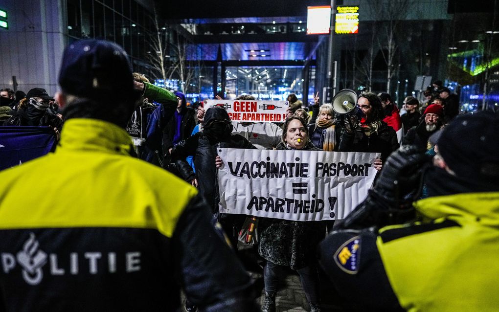 Protesterende mensen. Ze beschikken onder meer over een toeter. Iemand houdt een spandoek omhoog met daarop de tekst: ”Vaccinatiepaspoort = Apartheid!” 