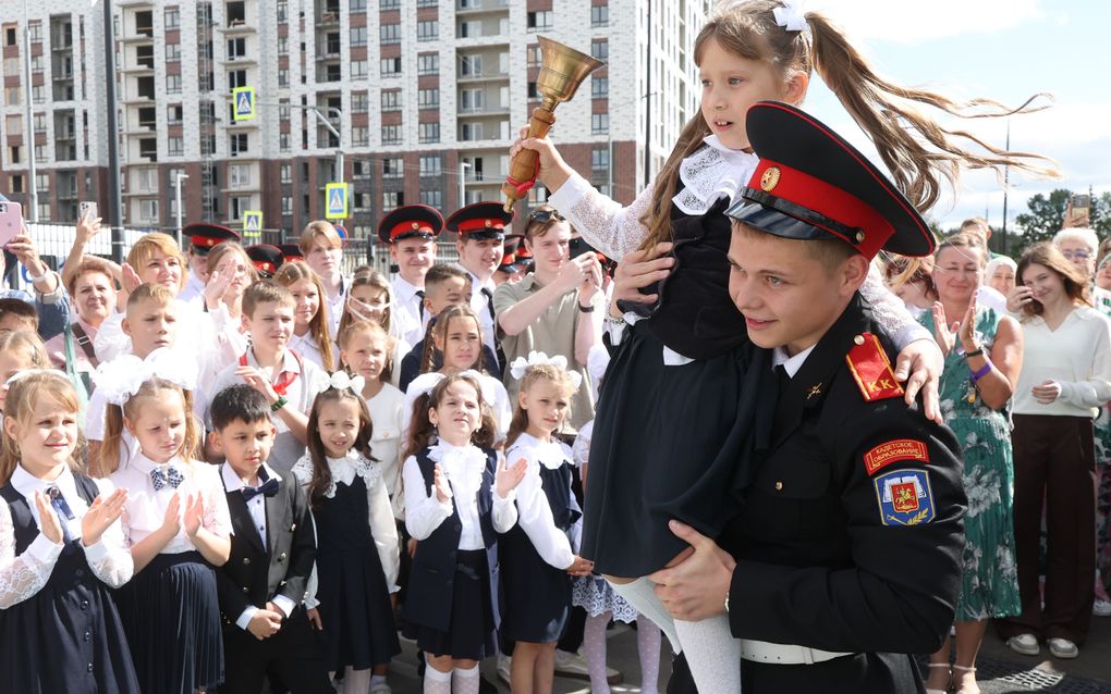 Kinderen kijken en klappen naar een jongen in uniform die een meisje draagt.