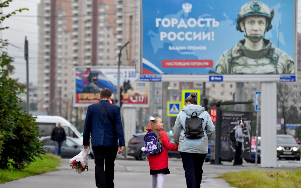 Drie mensen lopen over straat langs een billboard.