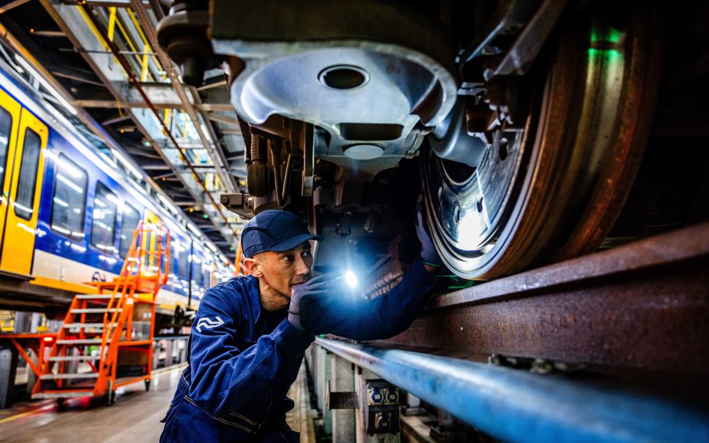 Een man in een blauw ketelpak schijnt met een lampje op een groot stalen wiel.