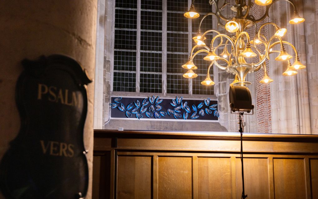 Het kunstwerk, 33 blauwe mosselen op een paneel onder een van de grote kerkramen. Op de voorgrond hangt een kroonluchter.