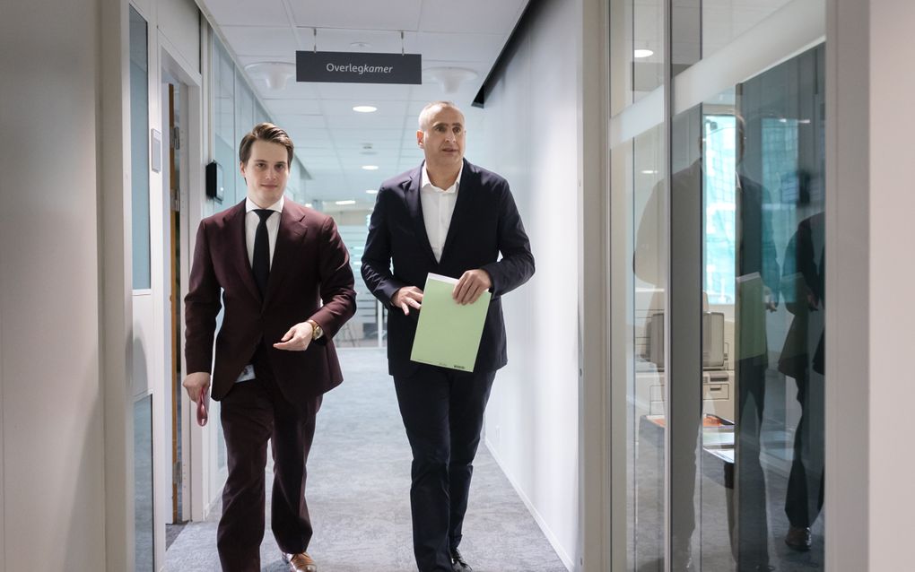 Twee heren in pak die in een van de gangen van het Tweede Kamergebouw wandelen.