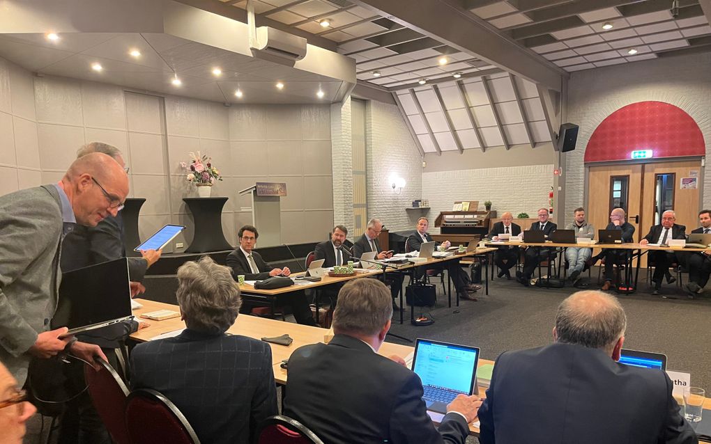 Mannen in donkere pakken achter een U-vormige vergadertafel.