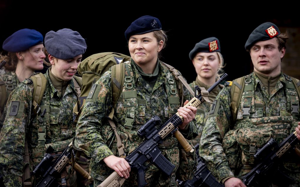 Jonge vrouw in uniform met een geweer in de hand tussen medestudenten.