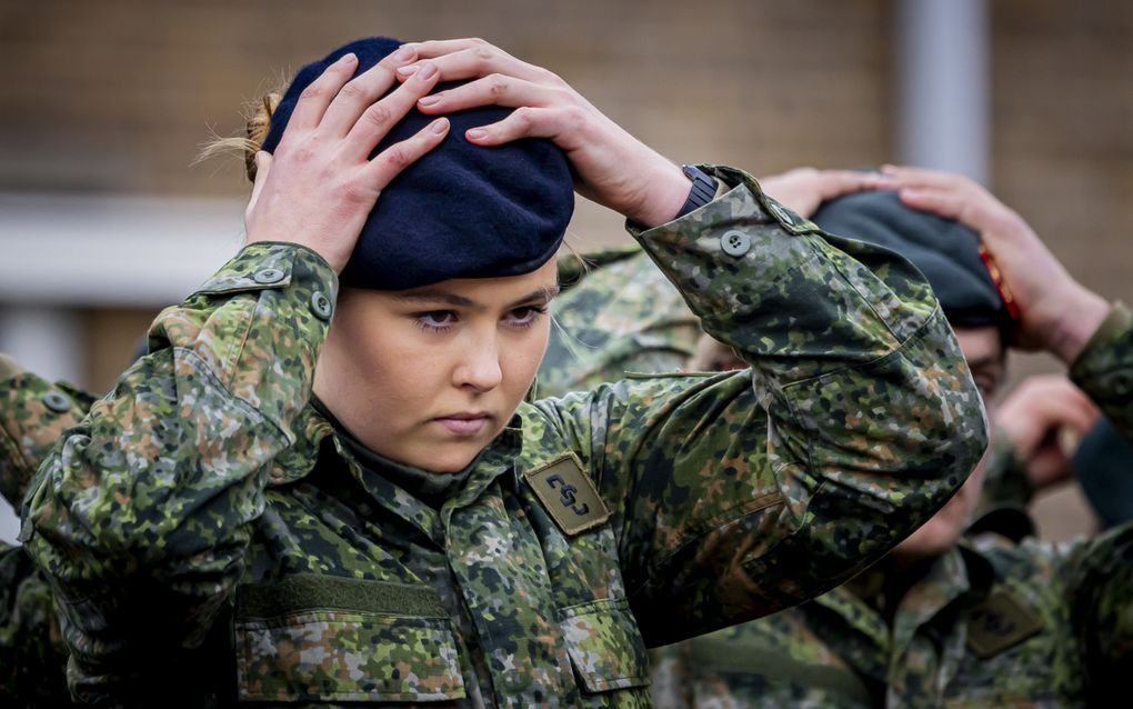 Jonge vrouw in militair uniform zet een blauwe baret op haar hoofd.