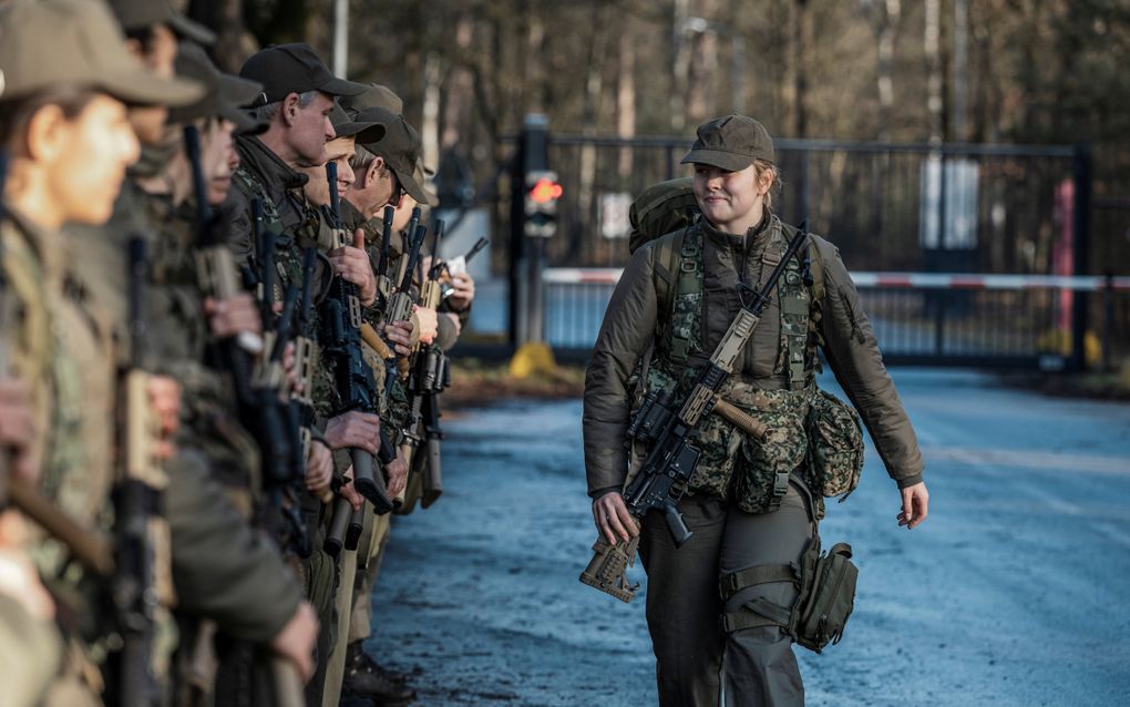 Een jonge vrouw in militair uniform loopt langs andere militairen die op een rij staan.