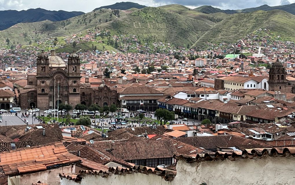 Stad met een kerk en huizen, op de achtergrond groene bergen.