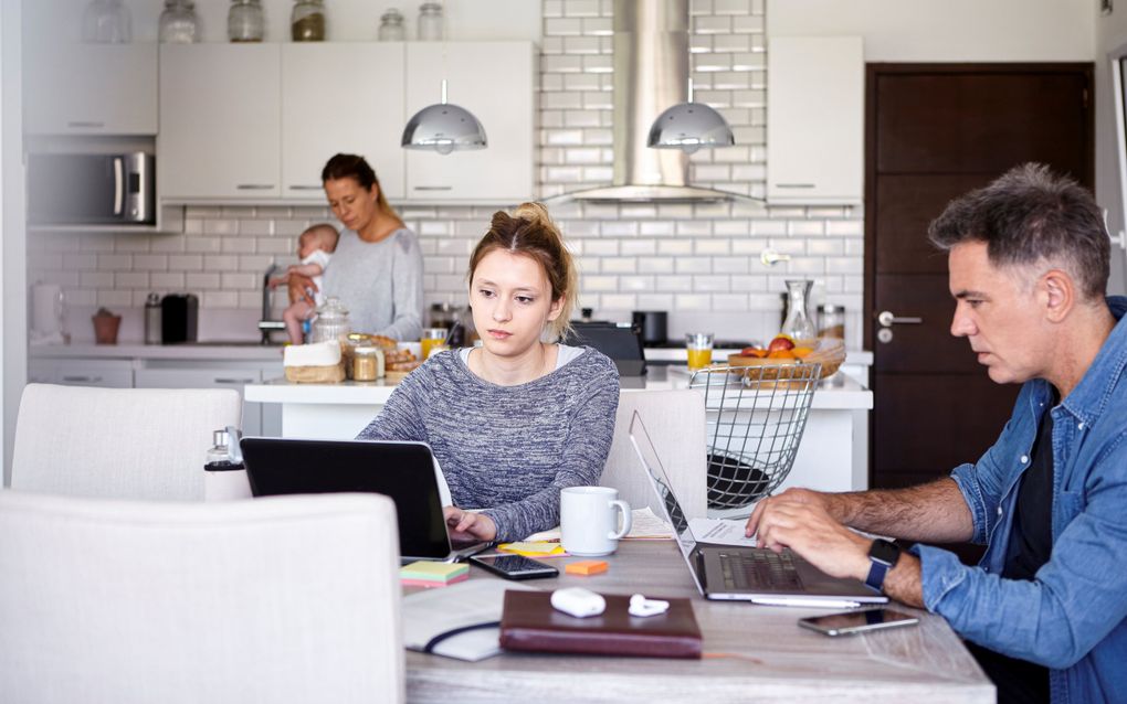 Diverse gezinsleden zijn in de keuken bezig met hun laptop of smartphone.
