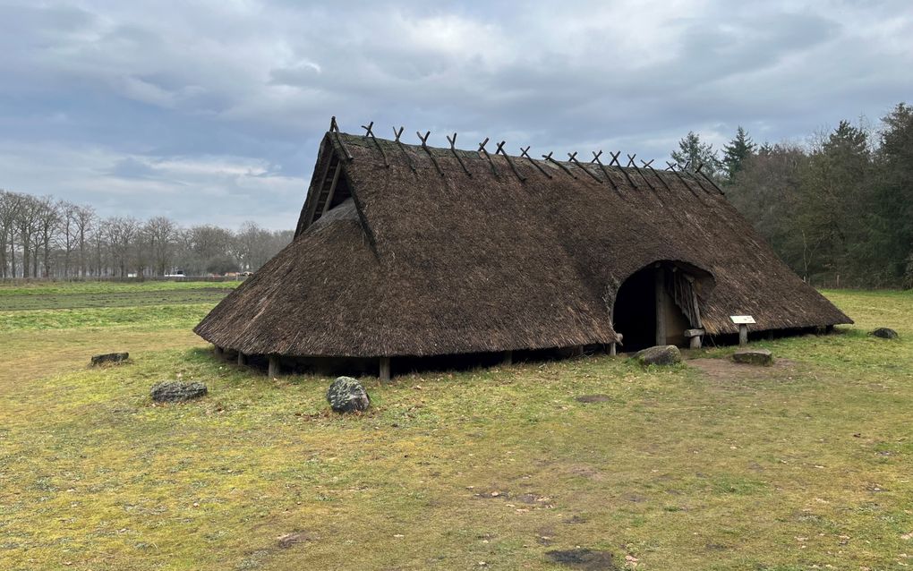 Een reconstructie van een boerderij uit de ijzertijd, met een rieten dak dat tot bijna op de grond loopt. Om de boerderij liggen wat grote keien.
