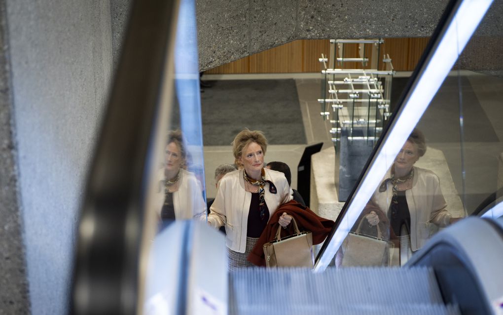 Vrouw met tas in haar hand en jas op haar arm op een roltrap in het Tweede Kamergebouw.