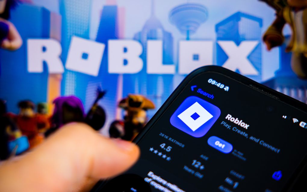 Een vinger boven een telefoonscherm met daarachter groot het logo van Roblox.