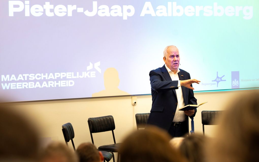 Een blanke man in een donker pak staat voor een menigte te presenteren.