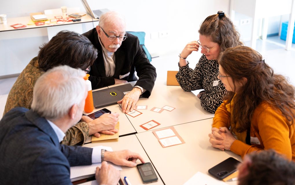 Een aantal mannen en vrouwen zitten rond een tafel en kijken naar kaartjes.