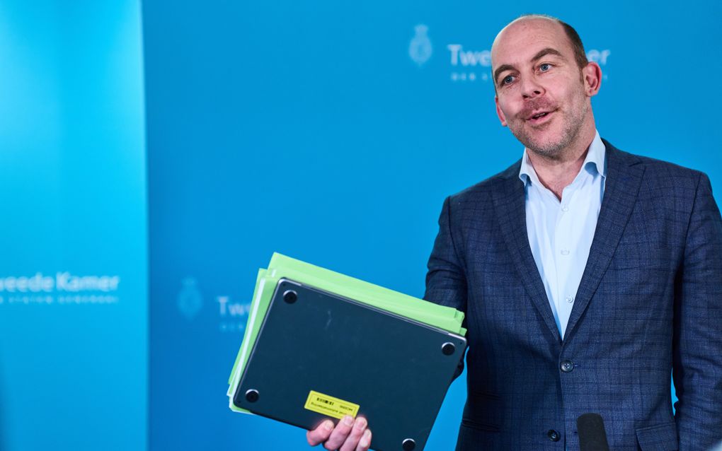 Man in pak staat met laptop en papieren in zijn hand.