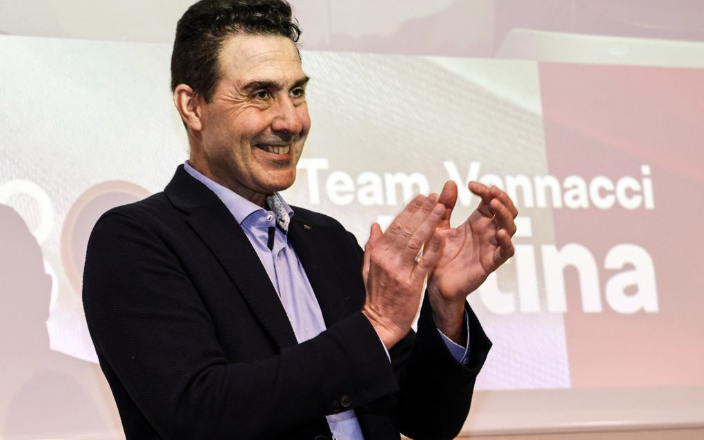 Een Italiaanse man met donker haar en donker pak met lichtblauw overhemd klapt lachend in zijn handen.