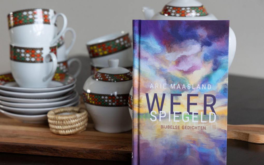 Een klein boekje met een veelkleurige omslag staat tegen wat serviesstukken aan. Links staan borden en kopjes gestapeld.