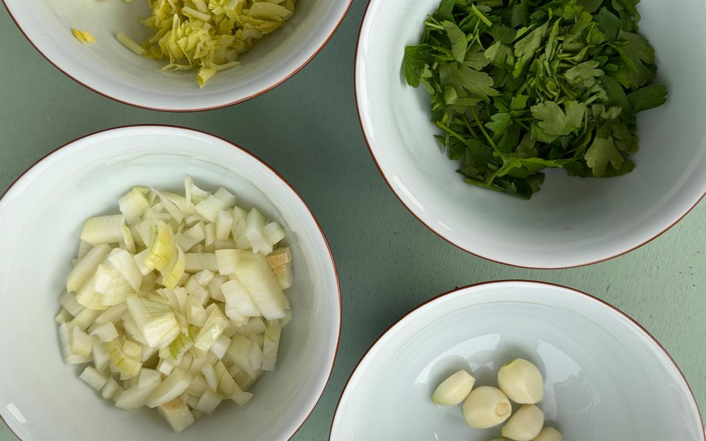 Vier witte schaaltjes. Met de klok mee: stukjes prei, steeltjes peterselie, vijf knoflooktenen en gesnipperde ui. 