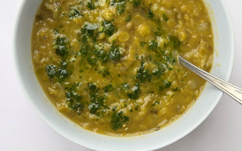 Een wit bord met daarin een geelgroene soep met een lepel erin.