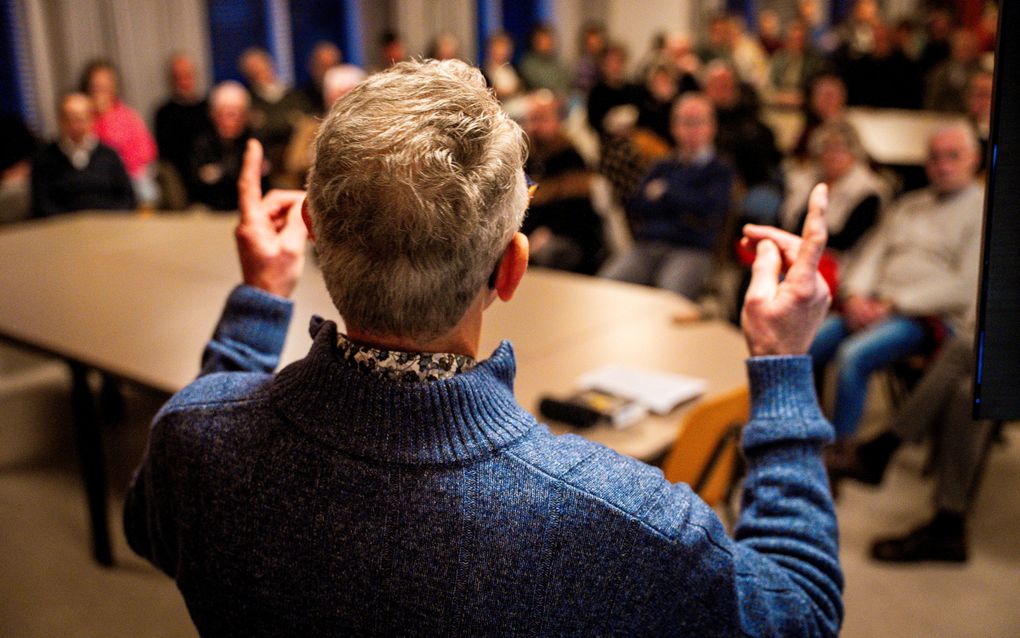 Man met vingers in de lucht voor een groep met mensen in een zaal.