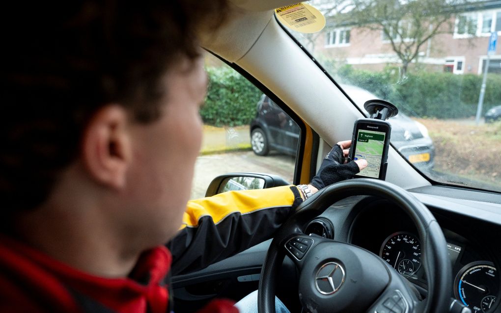 Een gezicht van een man die met zijn arm naar een telefoon reikt in de auto. 