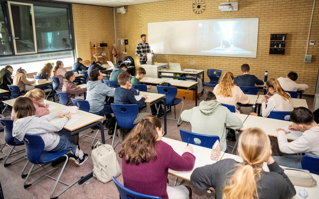 Een schoolklas vol jongens en meisjes met voorin een man en op het bord een AI-afbeelding waarop een man over de grond kruipt.