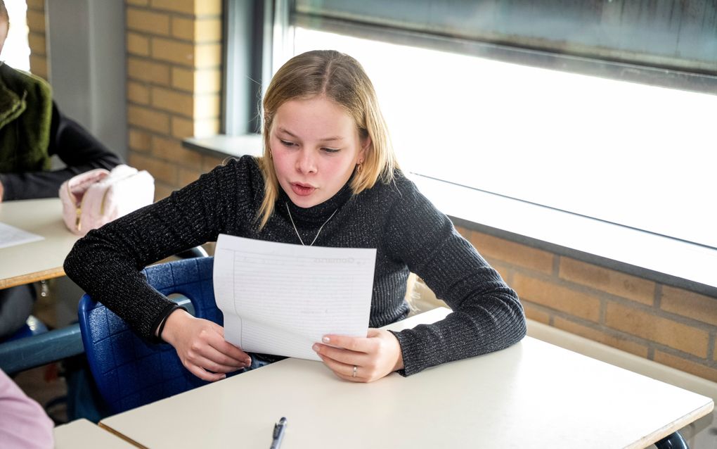 Een meisje leest iets voor van een wit vel papier.
