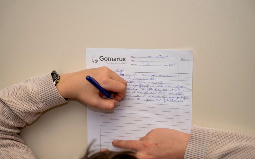 Een hand houdt een pen vast en schrijft op een wit lijntjespapier.
