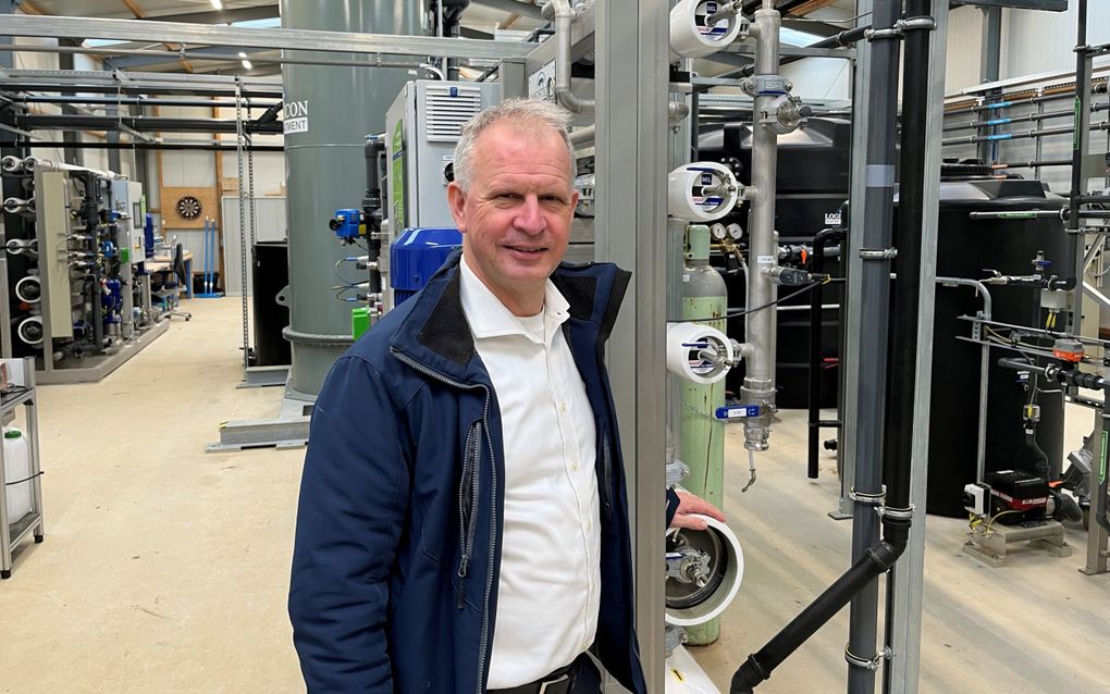 Een glimlachende man staat voor een technische installatie van buizen, vaten en kokers.