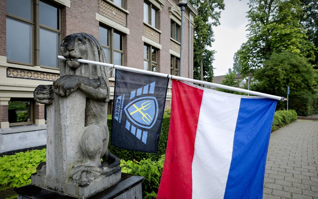Voor een gebouw staat een beeld van een leeuw. In de bek van de leeuw hangt een vlaggenstok met daaraan een omgekeerde Nederlandse vlag en een zwart-blauwe vlag met twee gele gestileerde hooivorken en de tekst Farmers Defence Force.