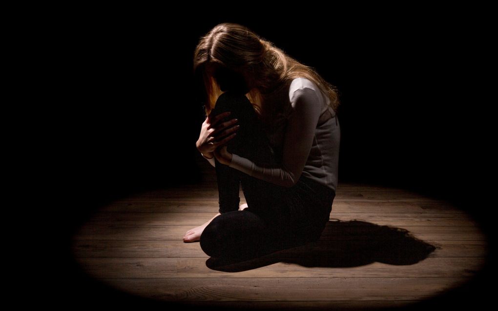 Meisje in halfduister knielt op planken vloer.