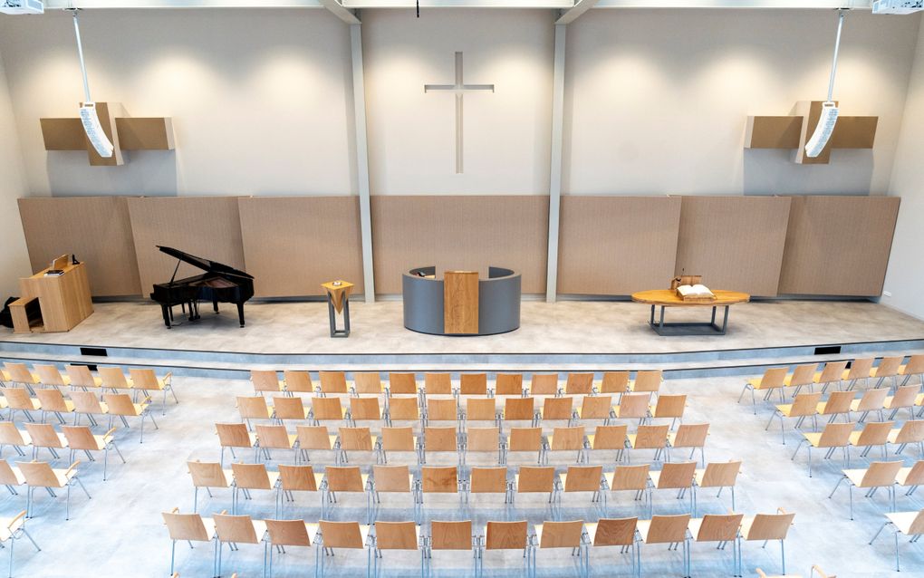 Op het podium de kansel, links ervan het doopvont en een vleugel; rechts een avondmaalstafel.