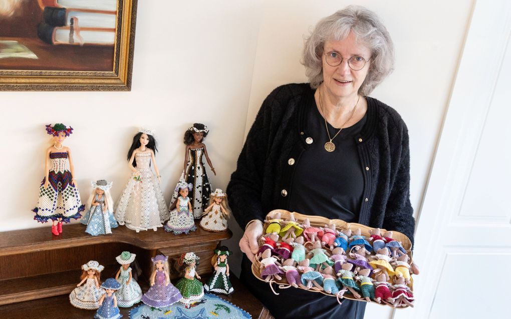 Mevrouw in zwarte kleding houdt dienblad vast met muisjes gemaakt van kralenwerk. Naast haar nog meer werkstukken.