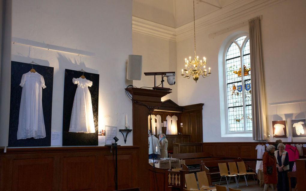 Aan de wanden van de kerk hangen doopjurken.