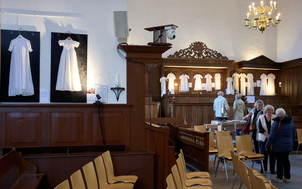 Oudere bezoekers lopen door de kerkruimte waarin de doopjurken te zien zijn.