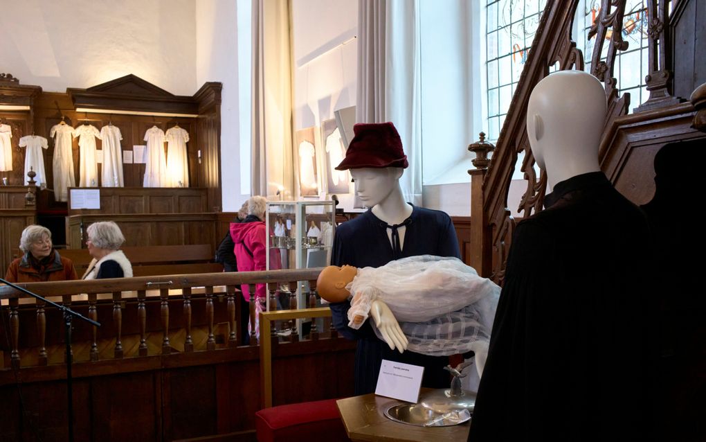 Twee paspoppen, de ene, een vrouw met een hoed op, draagt een dopeling.