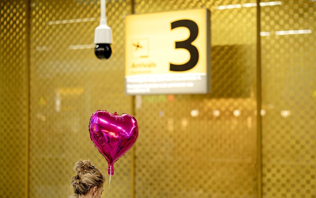 Een vrouw met een ballon in de vorm van een hart staat onder een bord met daarop het getal drie.
