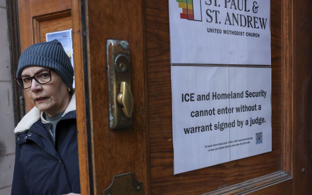 Een vrouw met muts bij een kerkdeur, met daarop een poster waarop onder meer staat dat de Amerikaanse immigratiedienst ICE en de Binnenlandse Veiligheidsdienst niet zomaar toegang hebben.