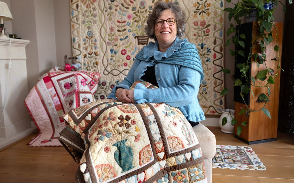 Vrouw in lichtblauwe trui zit op een bankje met een quilt over haar schoot.