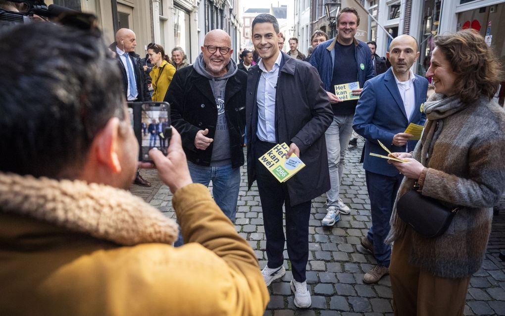 Man in blauwe jas met folders in zijn hand gaat op de foto met een man in zwarte jas.