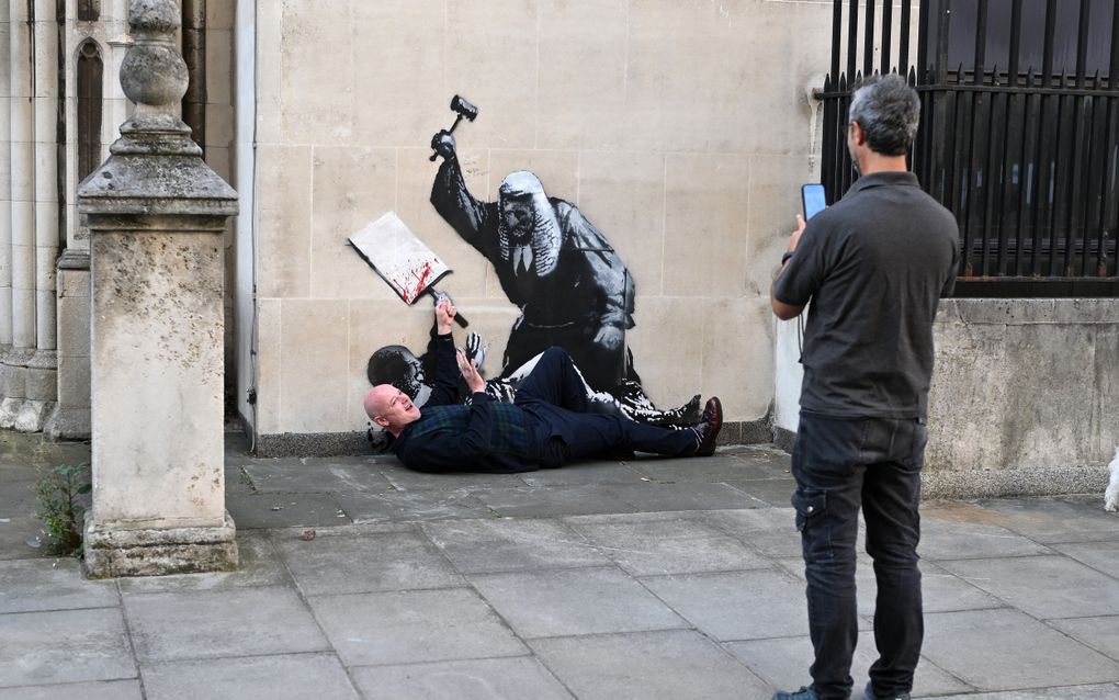 Een man maakt een foto van een man die op de grond ligt voor een kunstwerk.