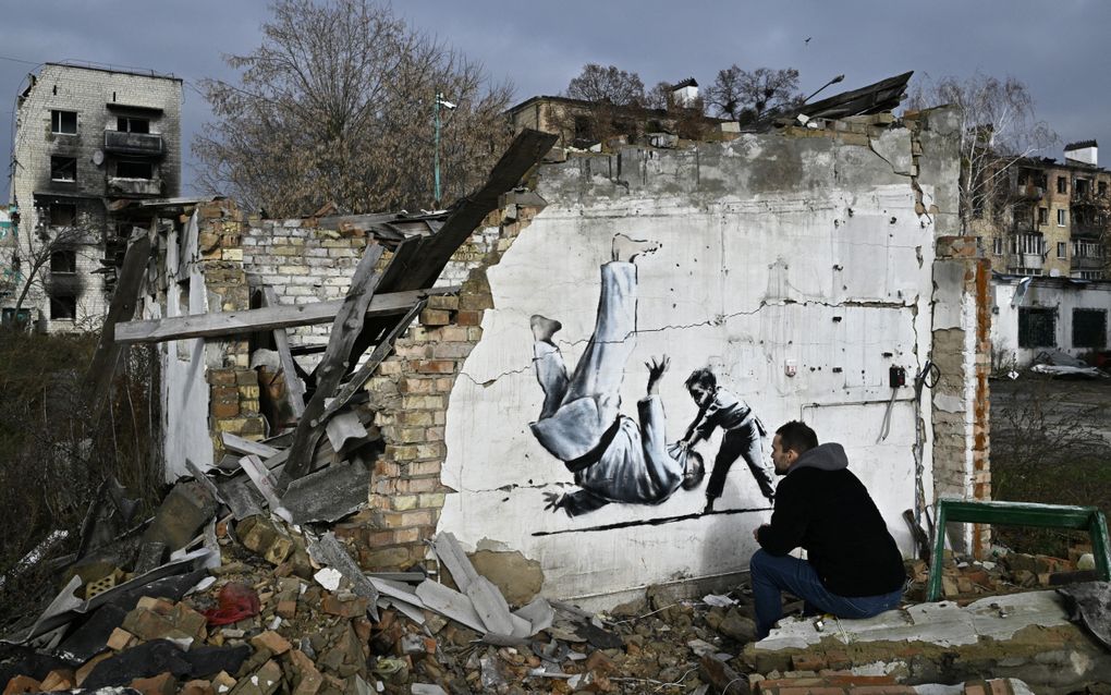 Een man zit in puin en kijkt naar een kunstwerk op een muur.