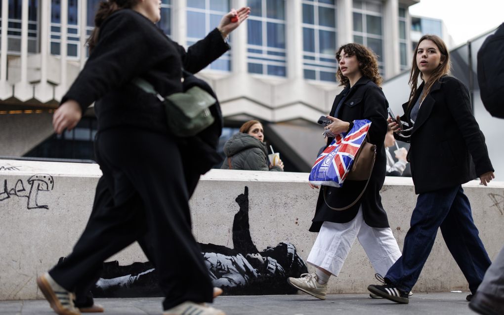 Vrouwen lopen langs een zwart-witafbeelding op een betonnen muurtje.