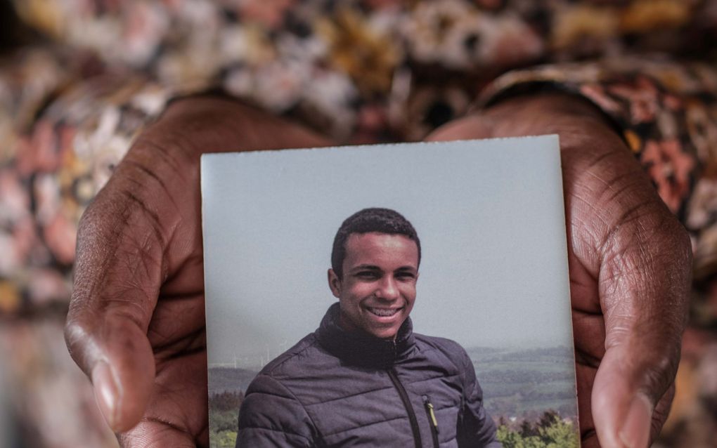 Handen van een kleurling met daarin een foto van een puber, glimlach met slotjesbeugel, donkerblauw jack aan.