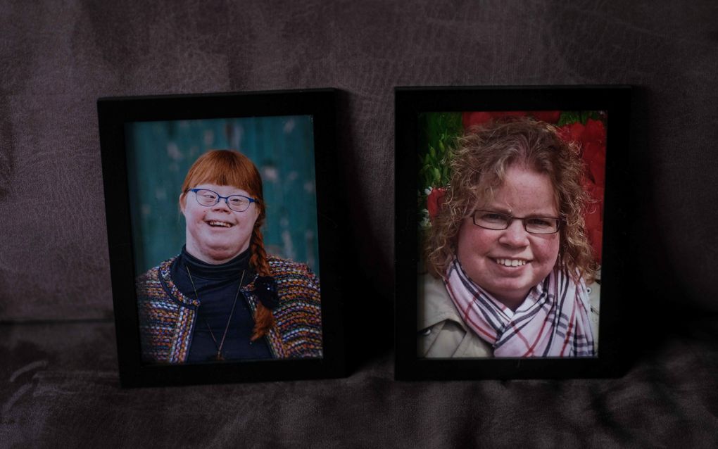 Twee fotolijstjes met links een foto van een meisje met rood haar in een vlecht. Ze heeft het syndroom van Down. Rechts een meisje met blond, kort krullend haar.