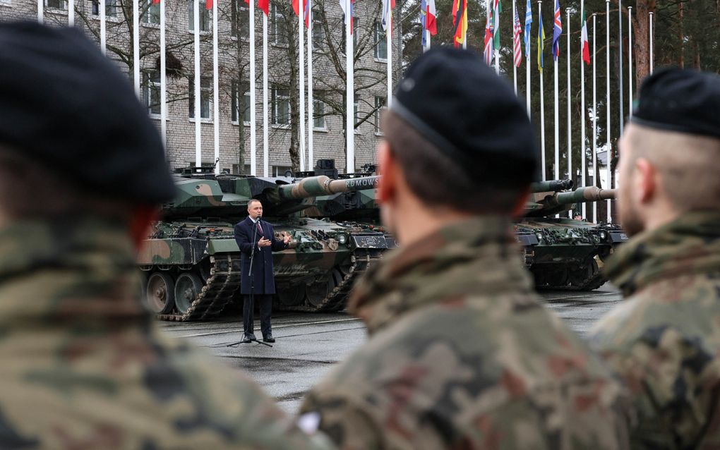 Man in kostuum voor pantservoertuigen spreekt militairen toe.