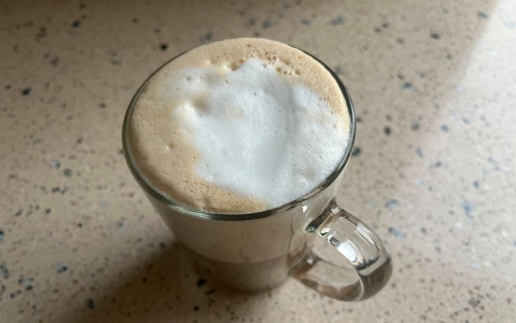 Een glas op een licht-granieten aanrecht. In het glas zit schuim dat grotendeels wit is, en aan de randen lichtbruin. Onderin het glas zit bruine vloeistof.