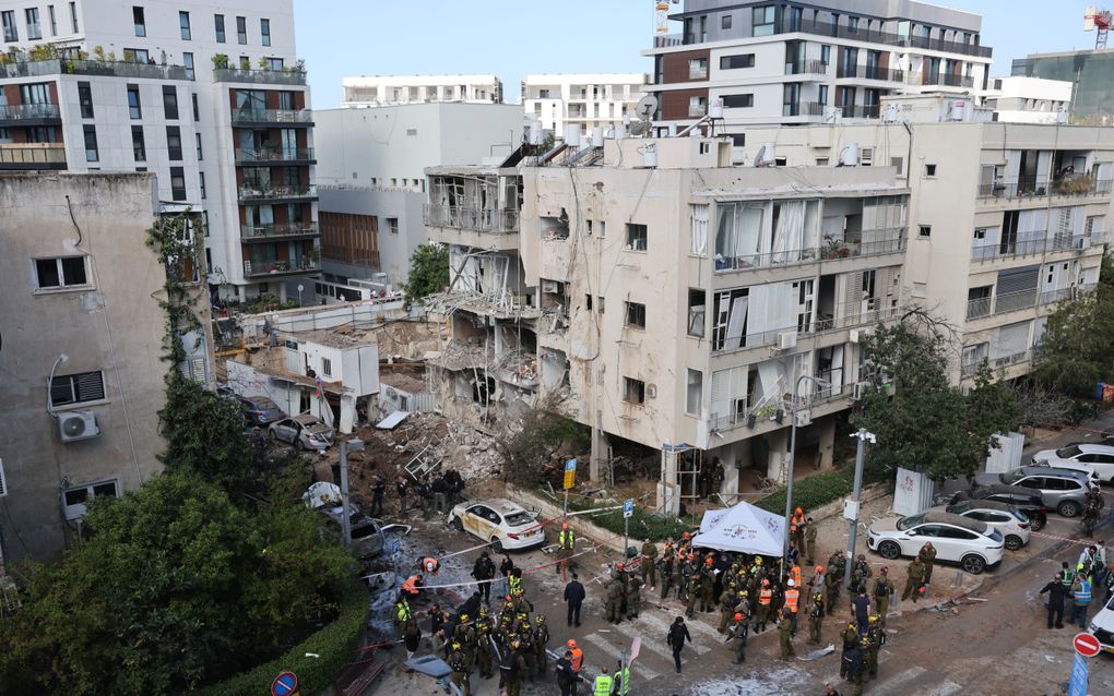 Luchtfoto van mensen in oranje en gele hesjes die naast een beschadigd gebouw hulp verlenen aan slachtoffers.