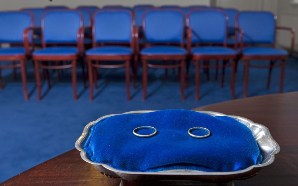 Twee ringen liggen op een blauw kussen op een tafel. Op de achtergrond staan enkele rijen blauwe stoelen.